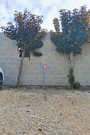 Ein Parkschild mit der Nummer 26, ein Kiesparkplatz und zwei Bäume mit Herbstlaub vor einer Steinmauer.