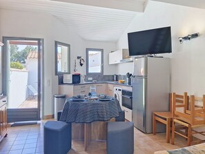 A compact kitchen with a dining area, a TV mounted on the wall, and a door leading to an outdoor area. - Les Dunes by Interhome (Ile d'Oléron)