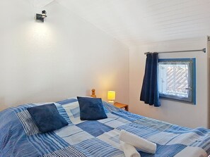 Ein Schlafzimmer mit einem Bett, einem Nachttisch, einer Lampe, einem Fenster mit Vorhängen und einer Wandleuchte.