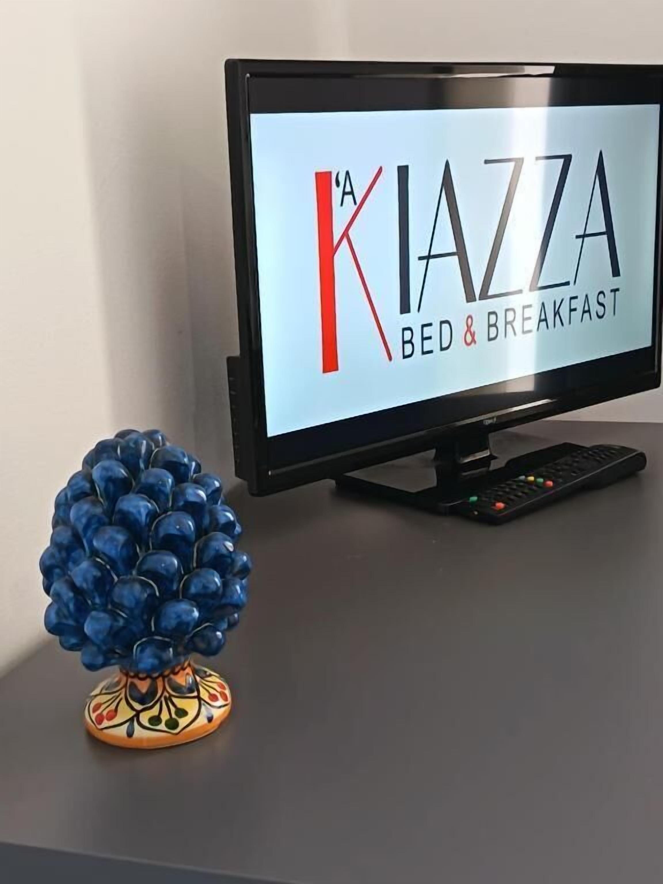 Televisiossa näkyy teksti ”A KIAZZA BED & BREAKFAST”, sen vieressä on kaukosäädin ja koristeellinen sininen esine.