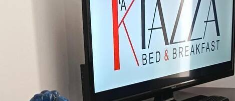Televisiossa näkyy teksti ”A KIAZZA BED & BREAKFAST”, sen vieressä on kaukosäädin ja koristeellinen sininen esine.