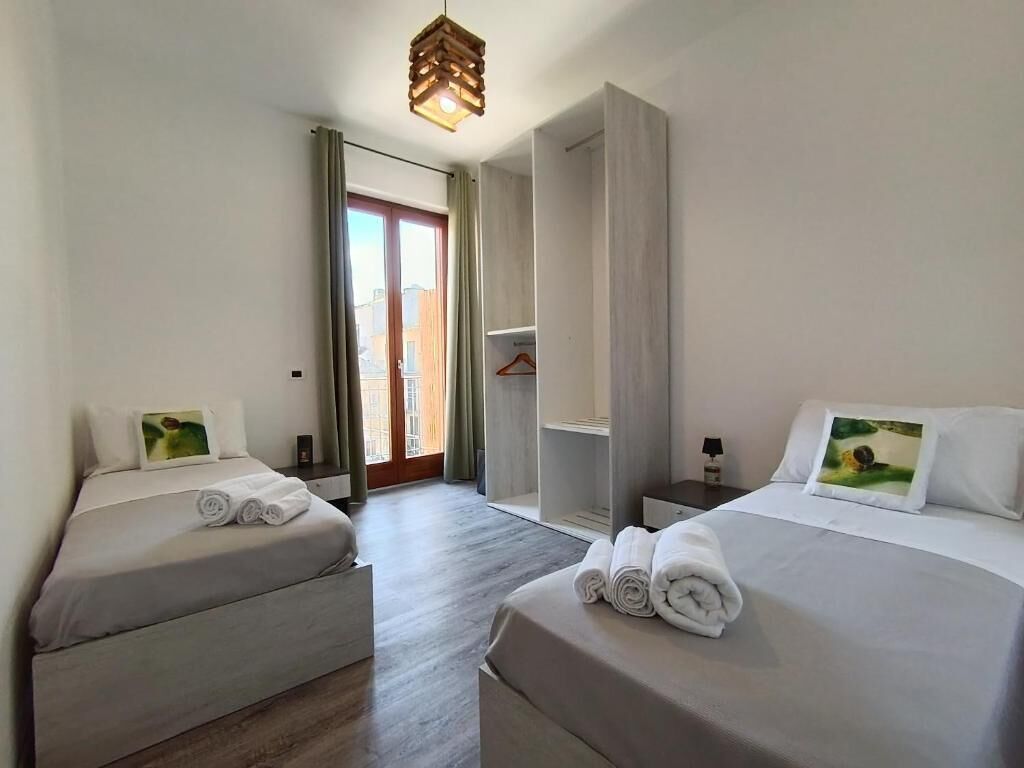 Habitación de hotel con dos camas, un armario, perchero y vistas a través de un ventanal.