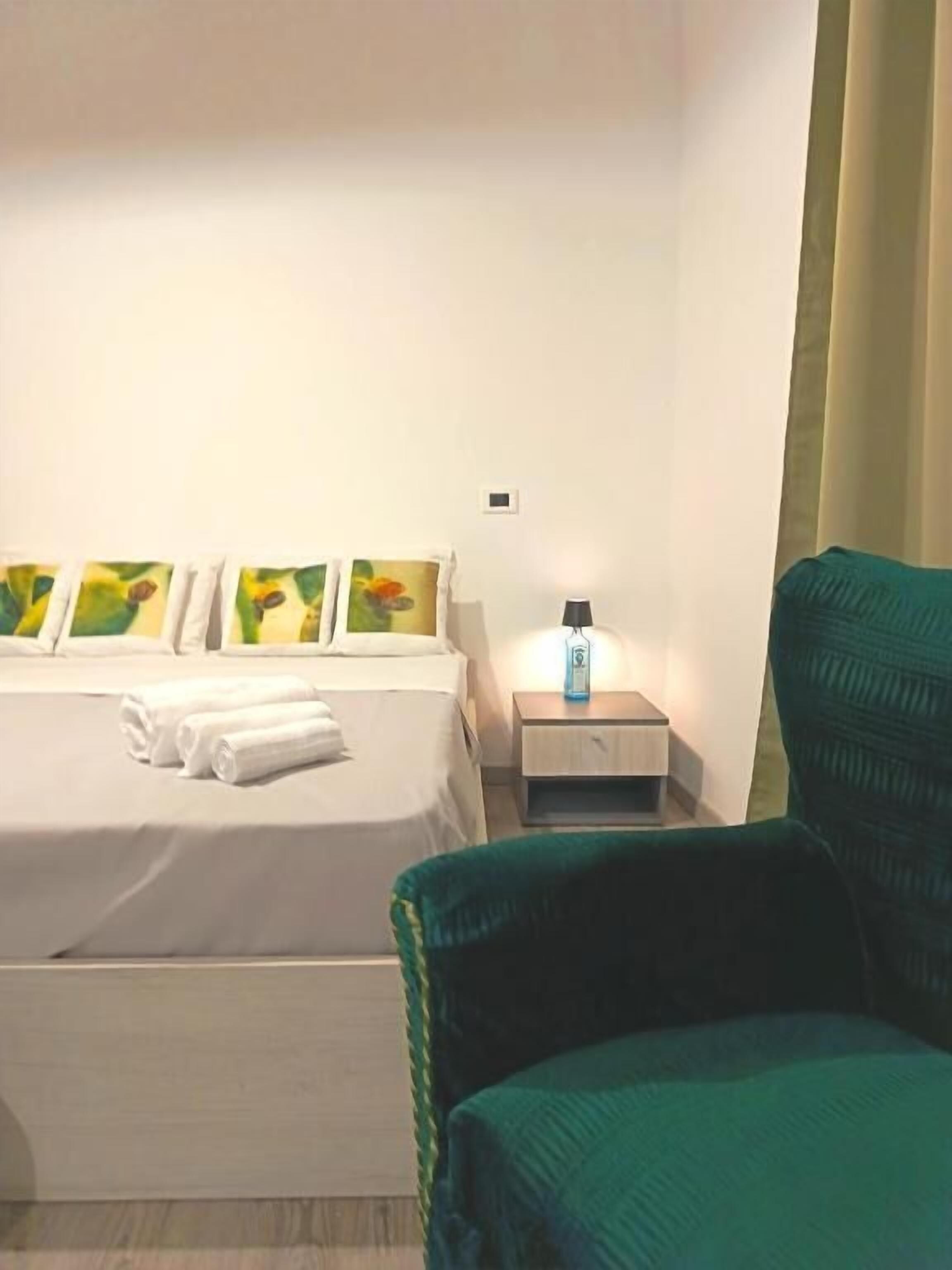 Et hotelværelse med en seng, et natbord med en lampe og en grøn stol.