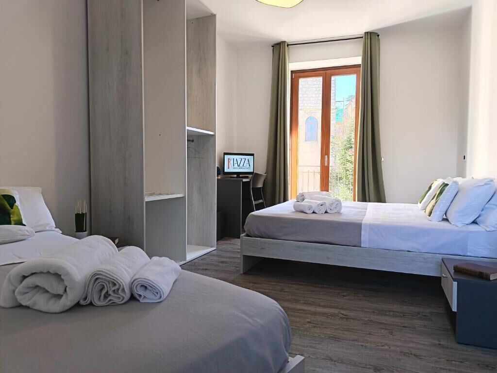 Quarto de hotel com duas camas, uma mesa com computador e vista para o exterior.