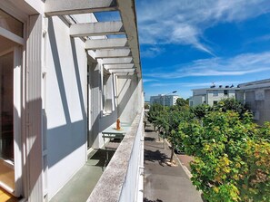 Ein Balkon mit Blick auf eine Straße, ein Gebäude mit weißer Fassade und einem klaren, blauen Himmel.