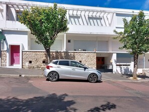 Ein weißes Auto steht auf einer Straße vor einem Gebäude mit einer Steinmauer und einer rosafarbenen Tür.