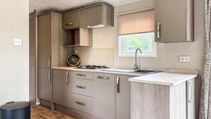 Cocina compacta con muebles de madera, estufa a gas, lavamanos y ventana con vistas.