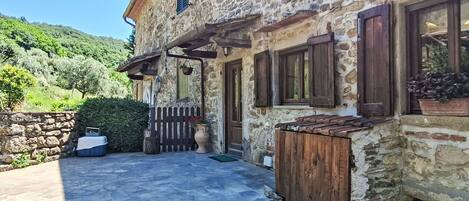 Una casa de piedra con patio de piedra, contraventanas de madera y cerca de madera.