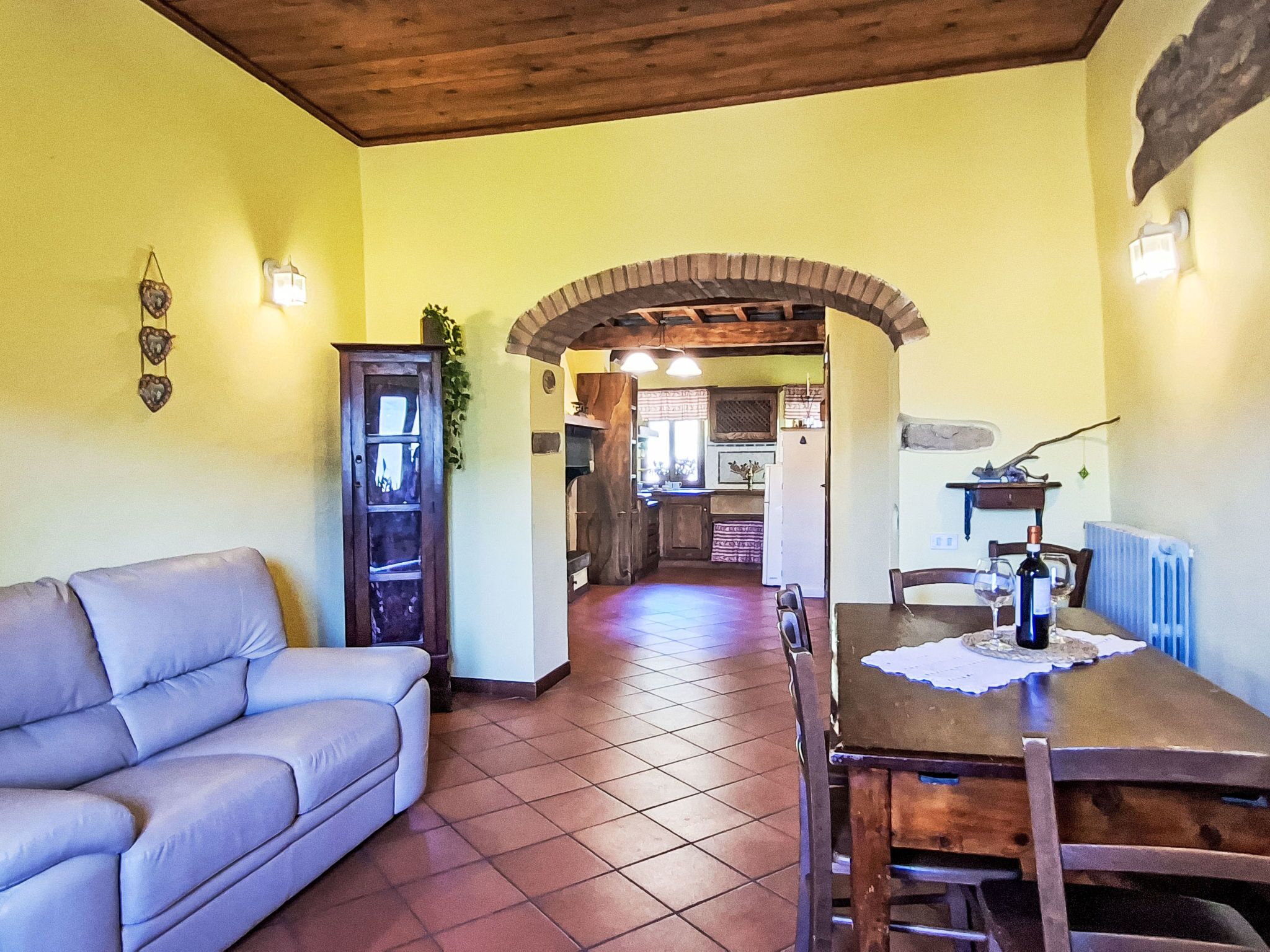 A cozy living room with a sofa, a dining table with chairs, a kitchen area, and a wooden ceiling.