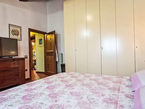 A bedroom with a bed, a dresser, a television, a wardrobe, and a door leading to another room. - Vacation home Luce by Interhome (Dicomano)