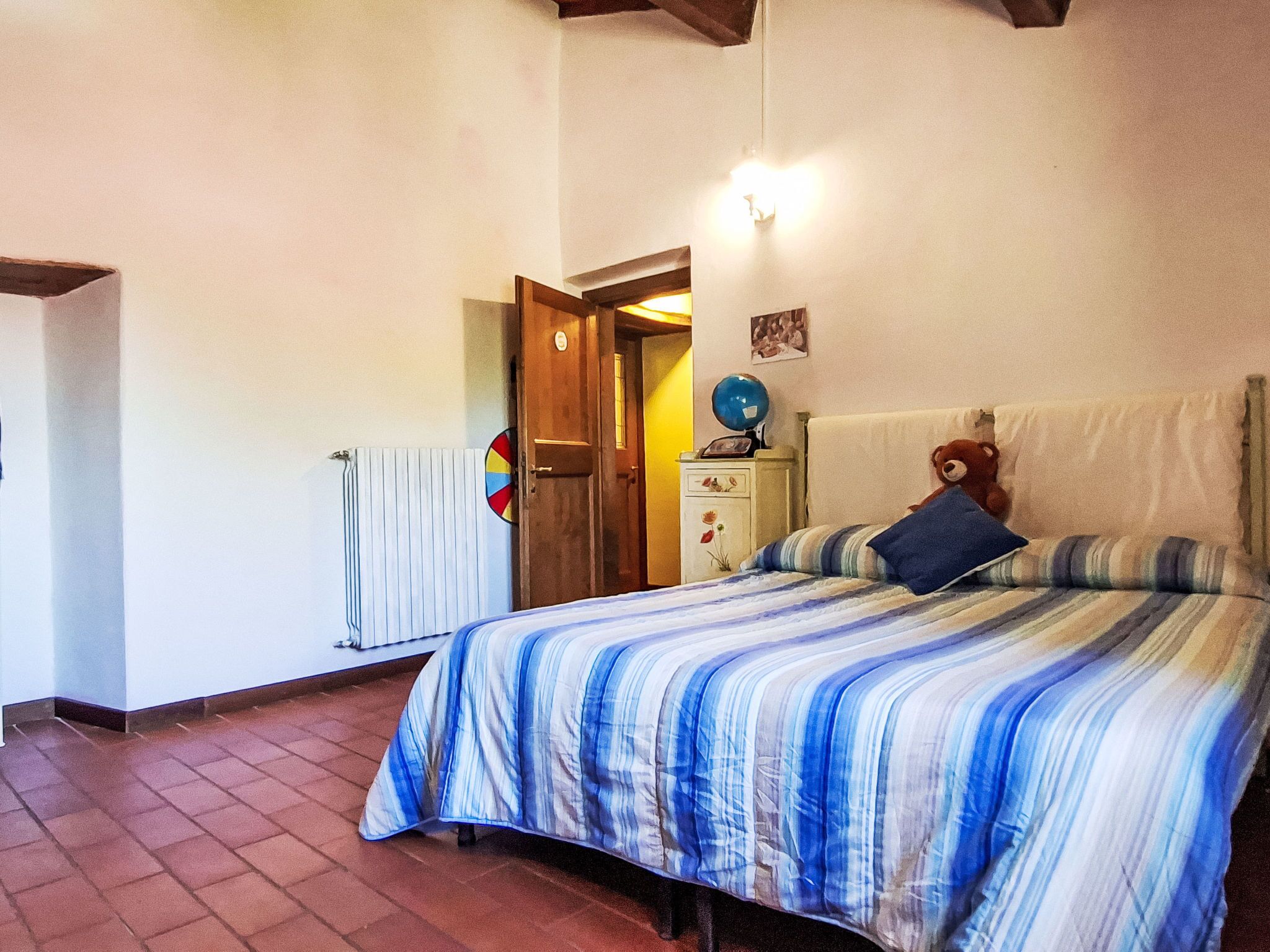 A bedroom with a bed, a dresser, a radiator, a door, and a wall-mounted globe.
