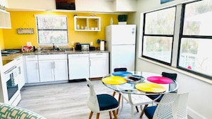 A kitchen with white cabinets, a white refrigerator, a window with a view, and a sign that says 'FRIENDS GATHER HERE'.