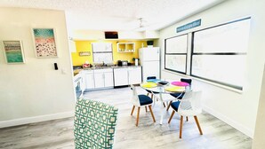 A modern kitchen with white cabinets, a dining area with colorful chairs, and a large window with artwork.