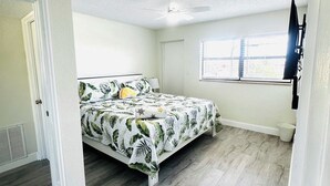 A bedroom with a bed, a ceiling fan, a window, and a door.