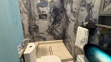 Een badkamer met toilet, bidet en wastafel met een marmeren achterwand.