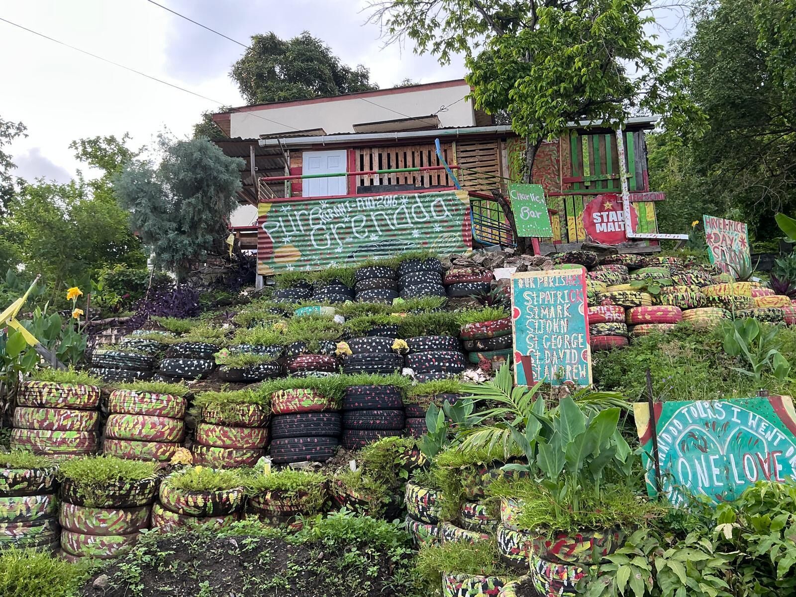 Un jardin agrémenté de jardinières faites avec des pneus et un bâtiment sur lequel est apposée une enseigne indiquant « Pure Green Garden ».