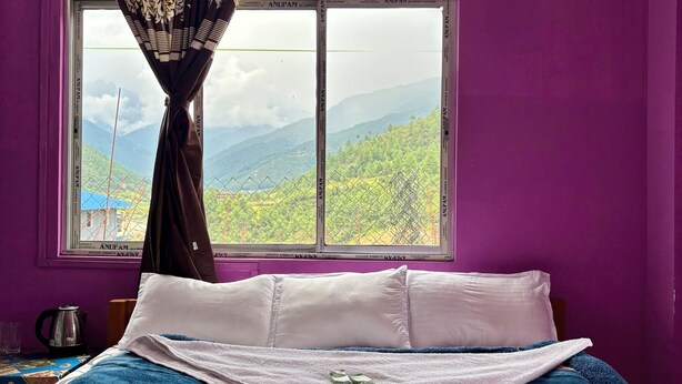 Ein Bett mit einer blauen und weißen Bettdecke, einem weißen Kopfkissen und einem schwarz-weißen Vorhang.