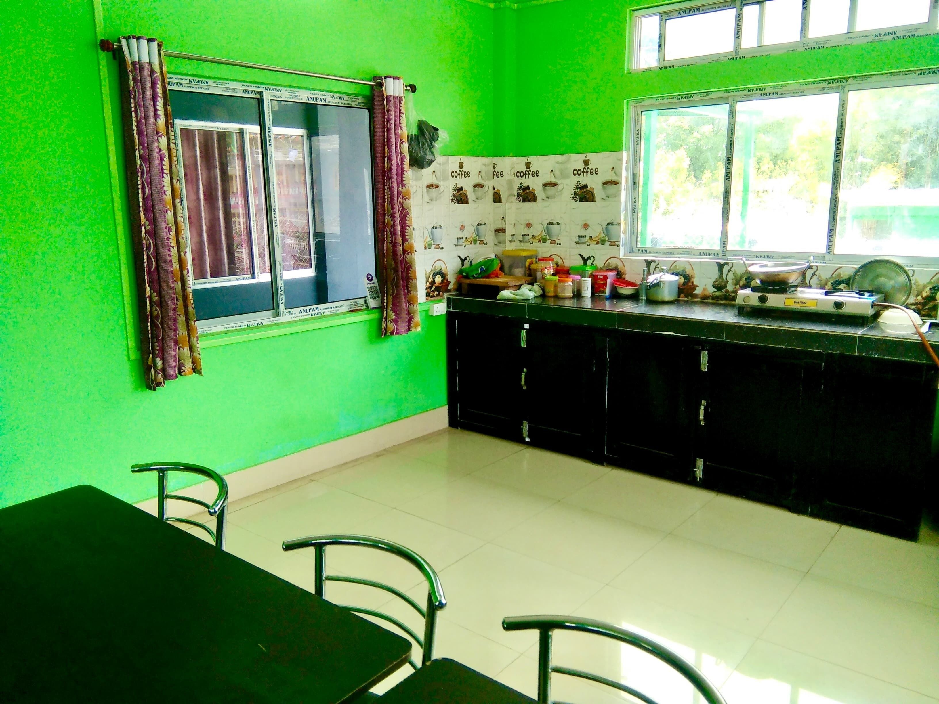 A kitchen with green walls, a dining table, chairs, and a window with curtains.