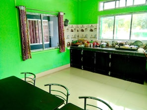 A kitchen with green walls, a dining table, chairs, and a window with curtains.