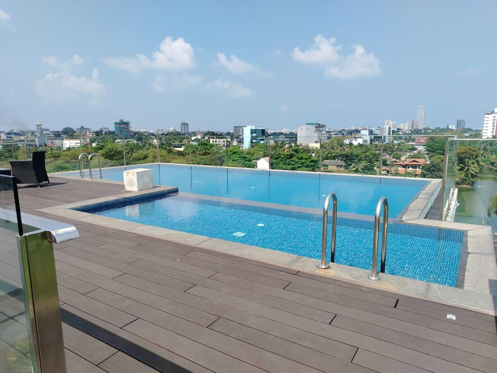 Ein Pool auf dem Dach mit Blick auf die Stadt, einer Holzterrasse und einem Metallgeländer.