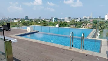 Ein Pool auf dem Dach mit Blick auf die Stadt, einer Holzterrasse und einem Metallgeländer.
