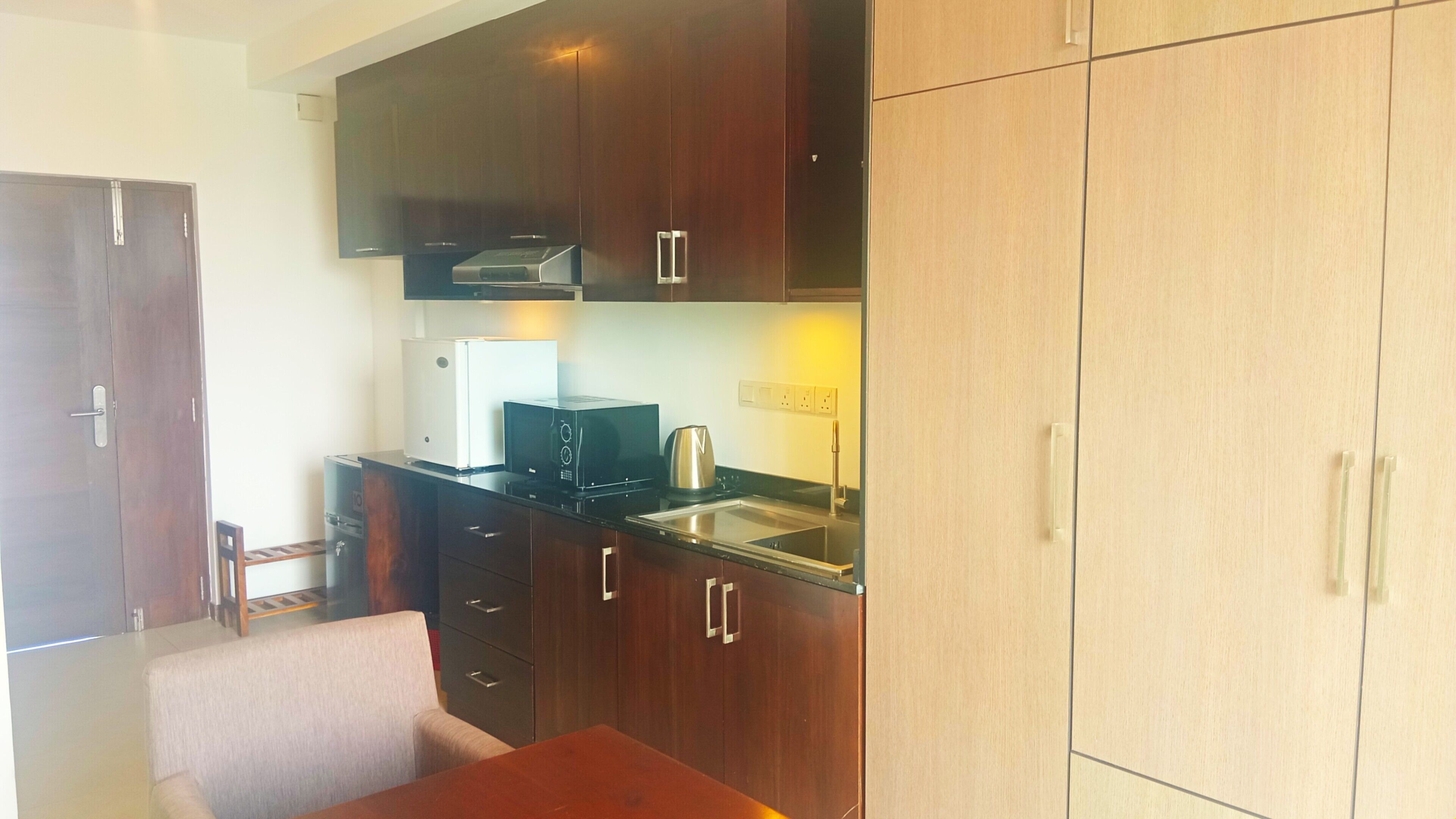 A compact kitchen with dark wood cabinets, a white refrigerator, a microwave, and a kettle on the countertop.