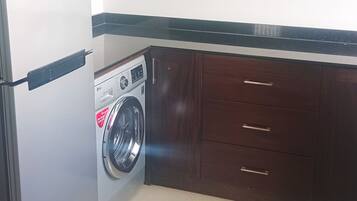 Una cocina con refrigerador de acero inoxidable, lavadora, armarios de madera y encimera negra.
