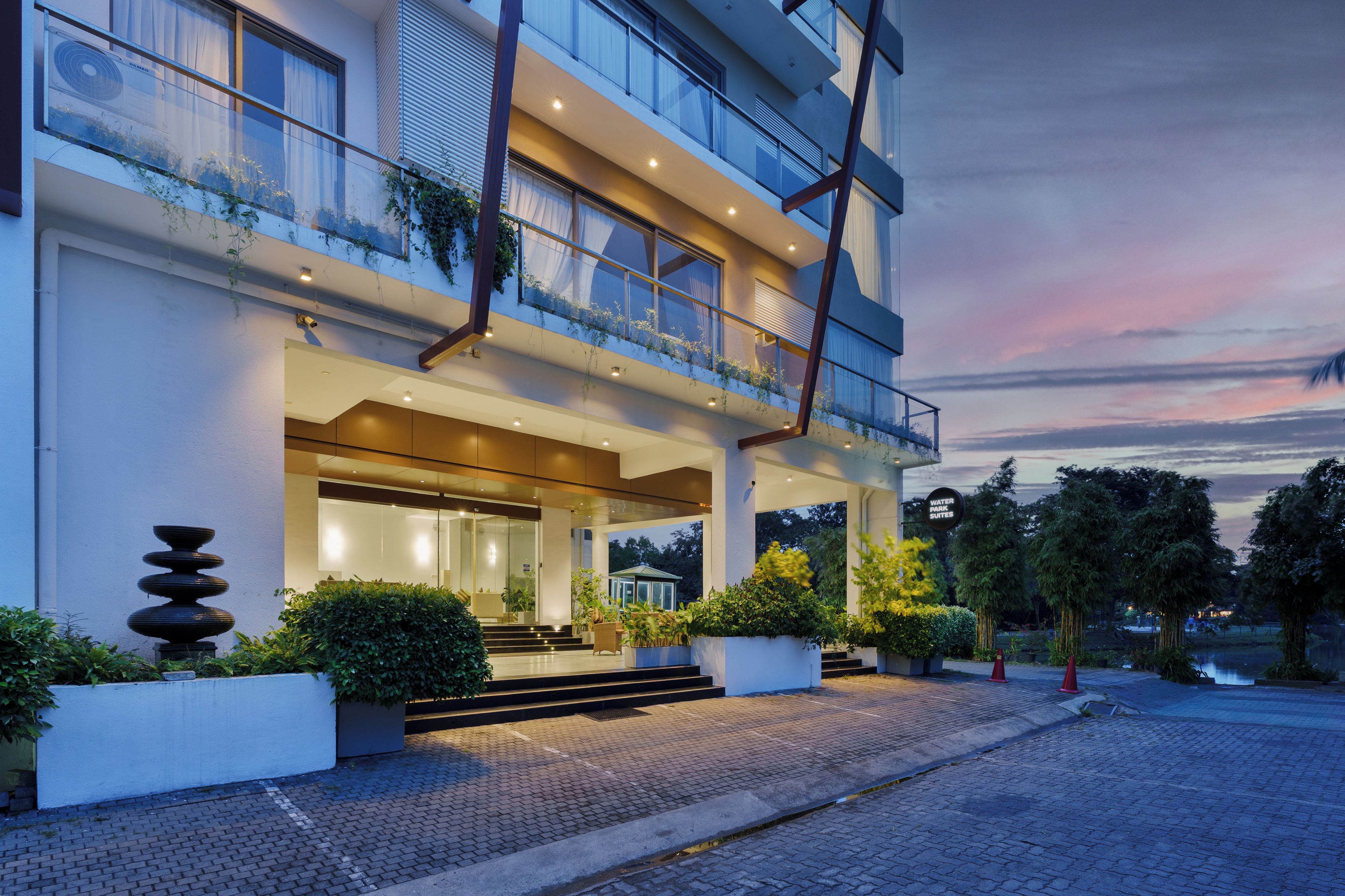 A modern hotel with a glass facade, outdoor seating area, and a water feature.