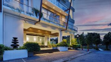 A modern hotel with a glass facade, outdoor seating area, and a water feature.