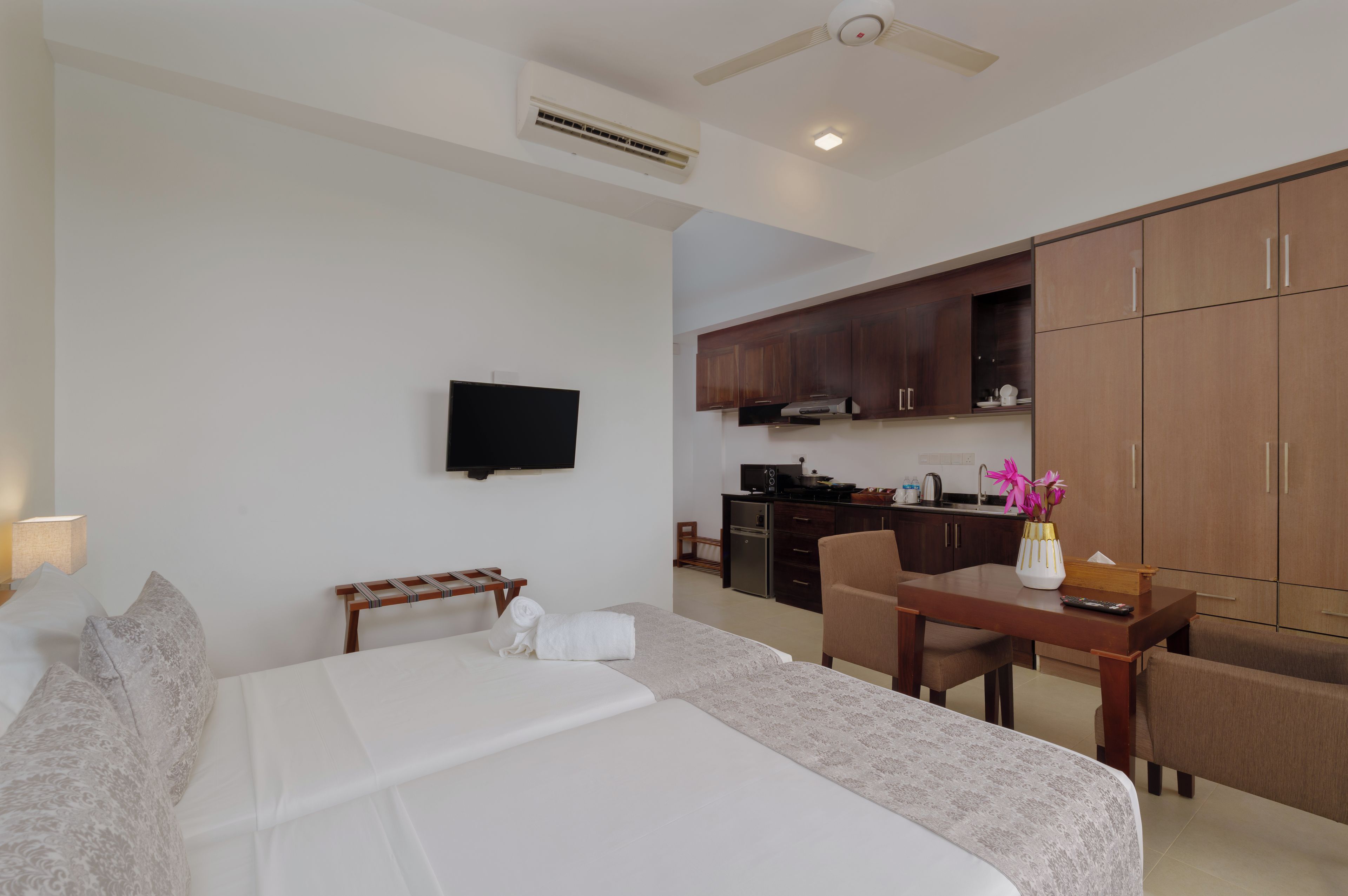 A hotel room with a bed, a desk, a chair, a television, and a kitchenette.