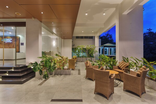 A hotel lobby with a reception desk, seating area with wicker furniture, and a view of the outside. - Water Park Suites (Nugegoda)