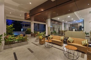 Un vestíbulo moderno con mobiliario de mimbre, plantas en macetas y vistas al exterior.