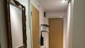 Un couloir avec un miroir, un lavabo, une porte, un radiateur et une chaise.