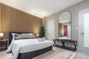 Un dormitorio moderno con cama, mesita de noche, lámpara, espejo y una planta.