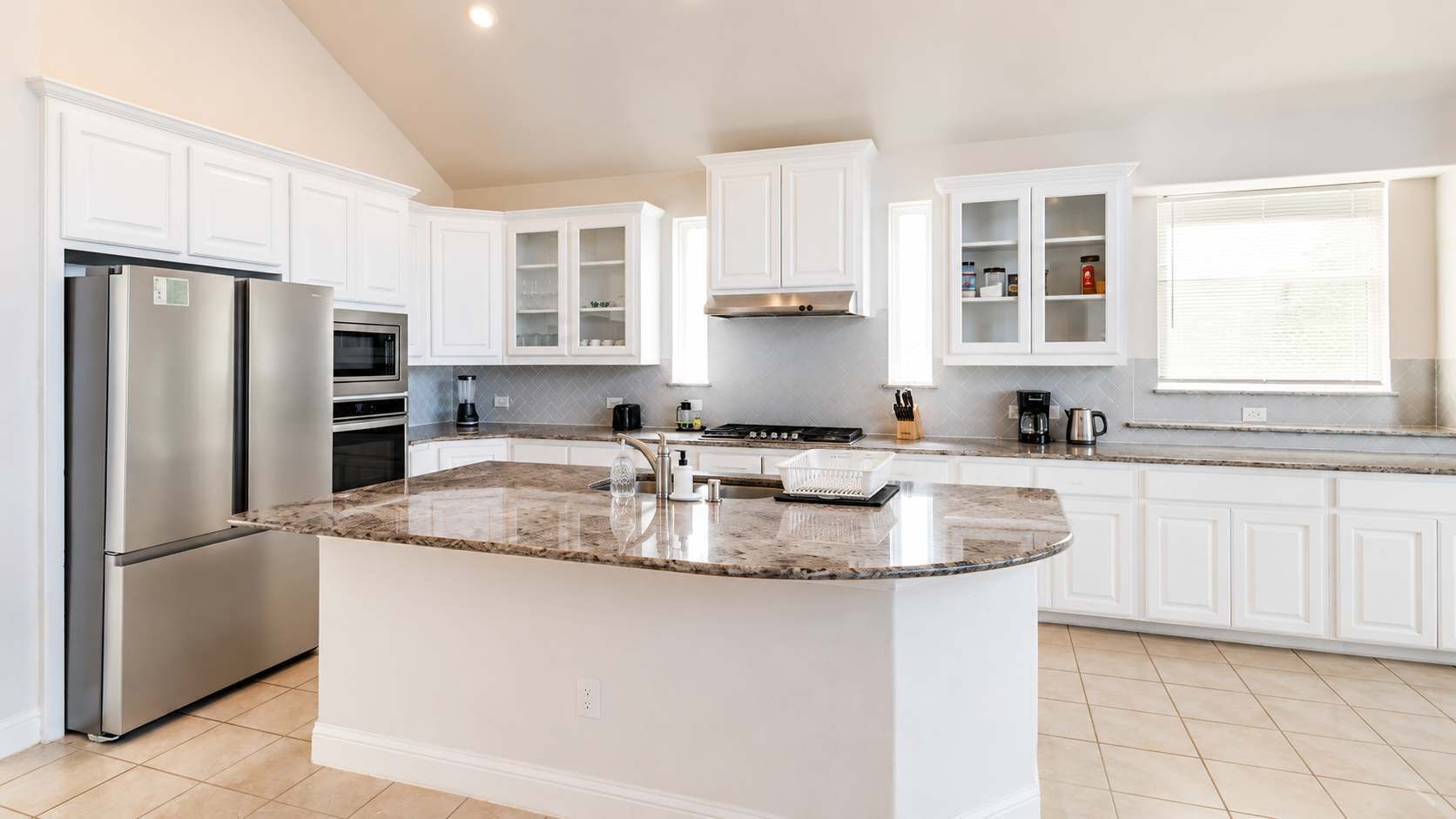 A modern kitchen with white cabinetry, a granite countertop island, stainless steel appliances, and a window providing natural light.
