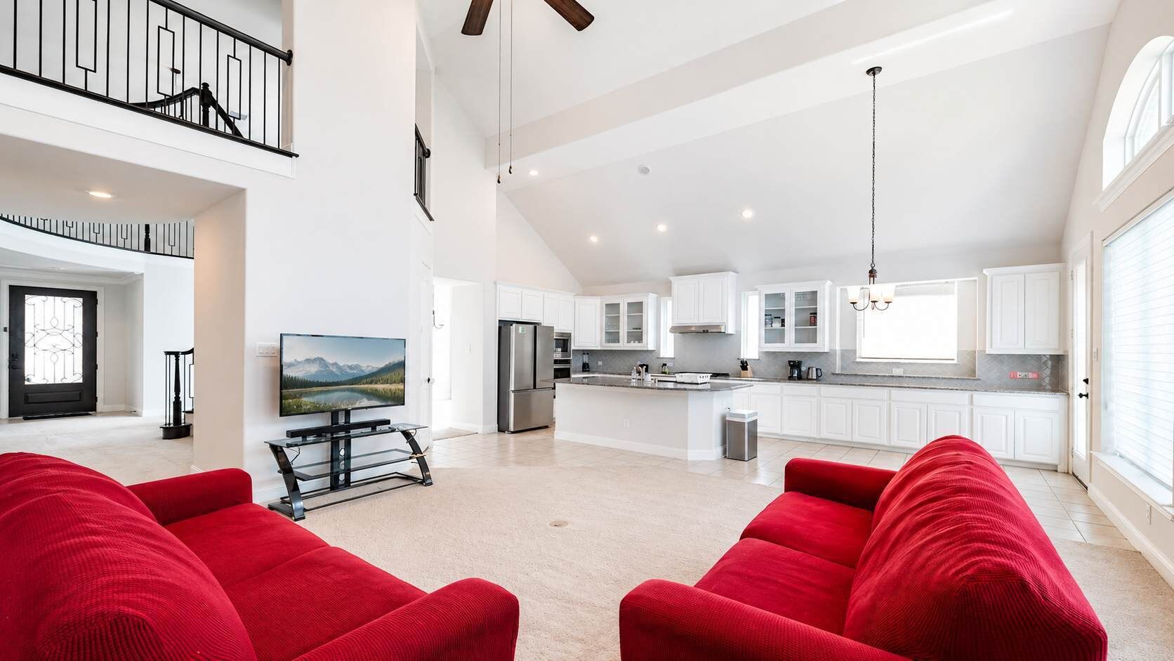 A spacious living area with a high ceiling, a kitchen with white cabinets, and a dining area with a table and chairs.