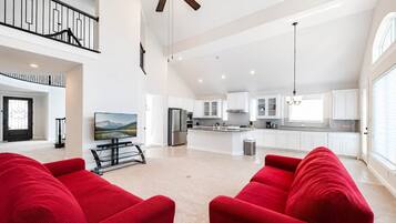 A spacious living area with a high ceiling, a kitchen with white cabinets, and a dining area with a table and chairs.