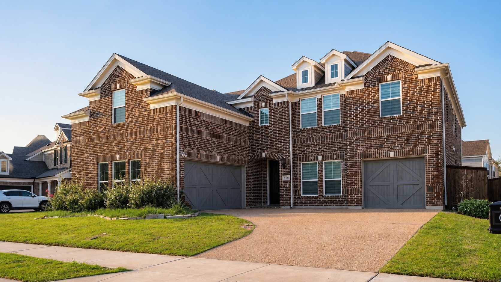 A two-story brick house with a garage, a driveway, and a lawn.