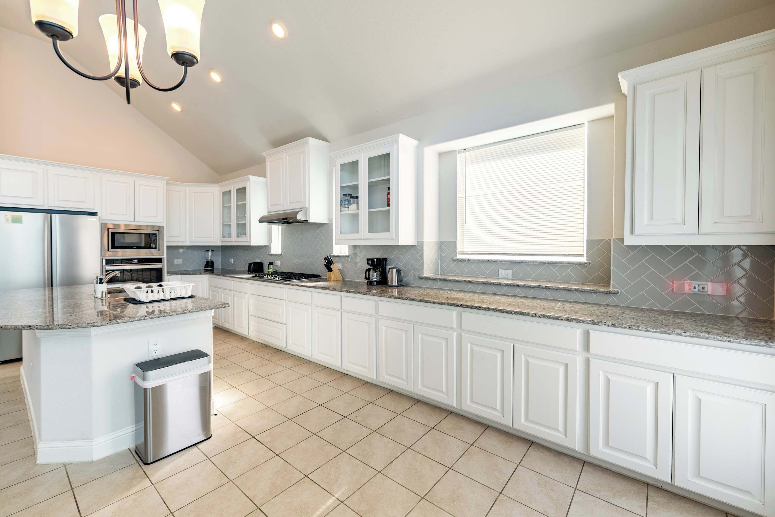 A kitchen with white cabinets, a stainless steel refrigerator, a microwave, a stove, and a trash can.