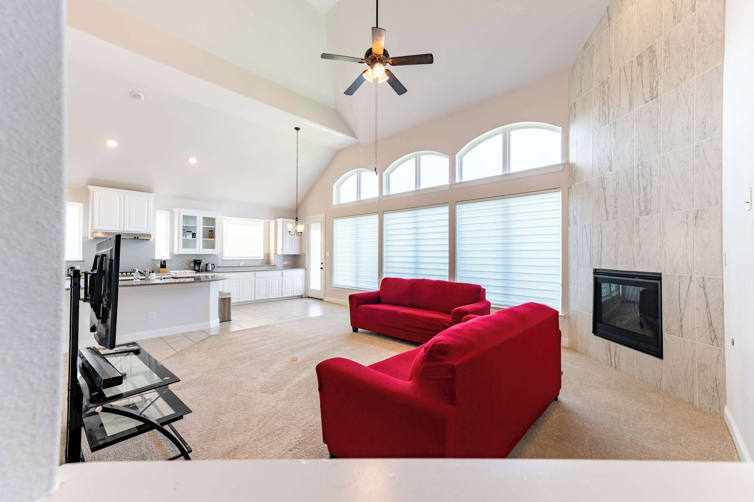 A spacious living area with a fireplace, red sofas, and a modern kitchen in the background.