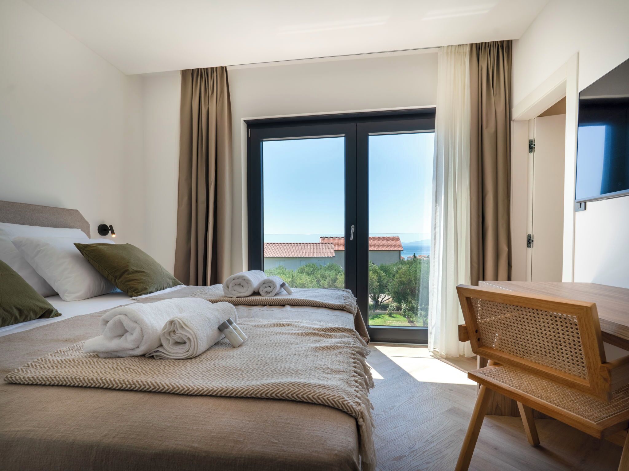 A hotel room with two beds, a desk, and a view of the sea.