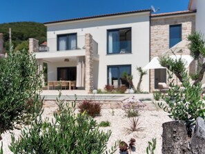 Ein zweistöckiges Haus mit Balkon, einer Steinfassade und einem Garten mit verschiedenen Pflanzen.