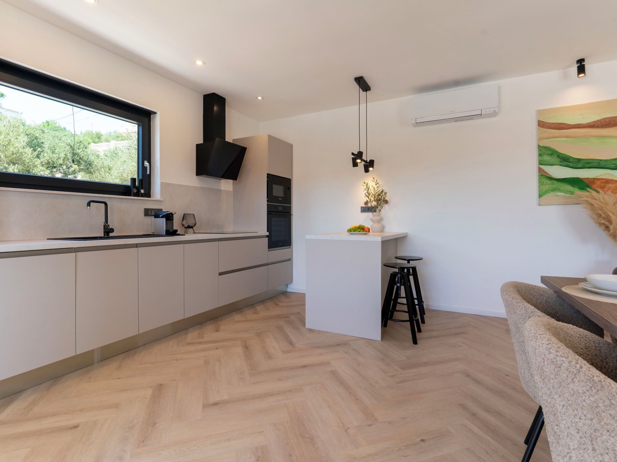 A modern kitchen with a herringbone floor pattern, a large window, and a dining area with a white island and black stools.