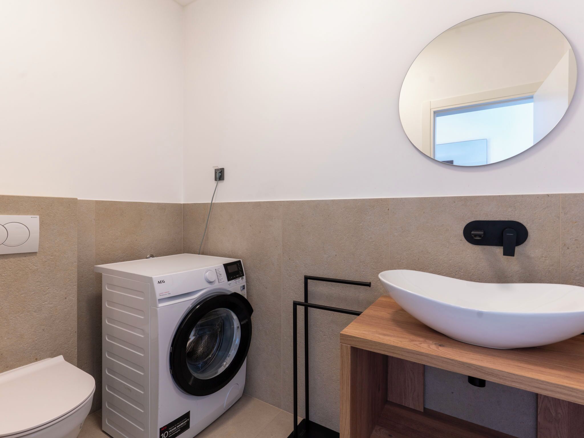 A compact bathroom with a front-loading washing machine, a toilet, and a sink with a wooden countertop.