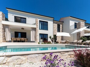 Ein modernes, zweistöckiges Haus mit Swimmingpool, Sitzgelegenheiten im Freien und einer Stein-Fassade.