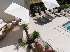 Área à beira da piscina com espreguiçadeiras, guarda-sóis, uma piscina pequena e plantas em vasos.