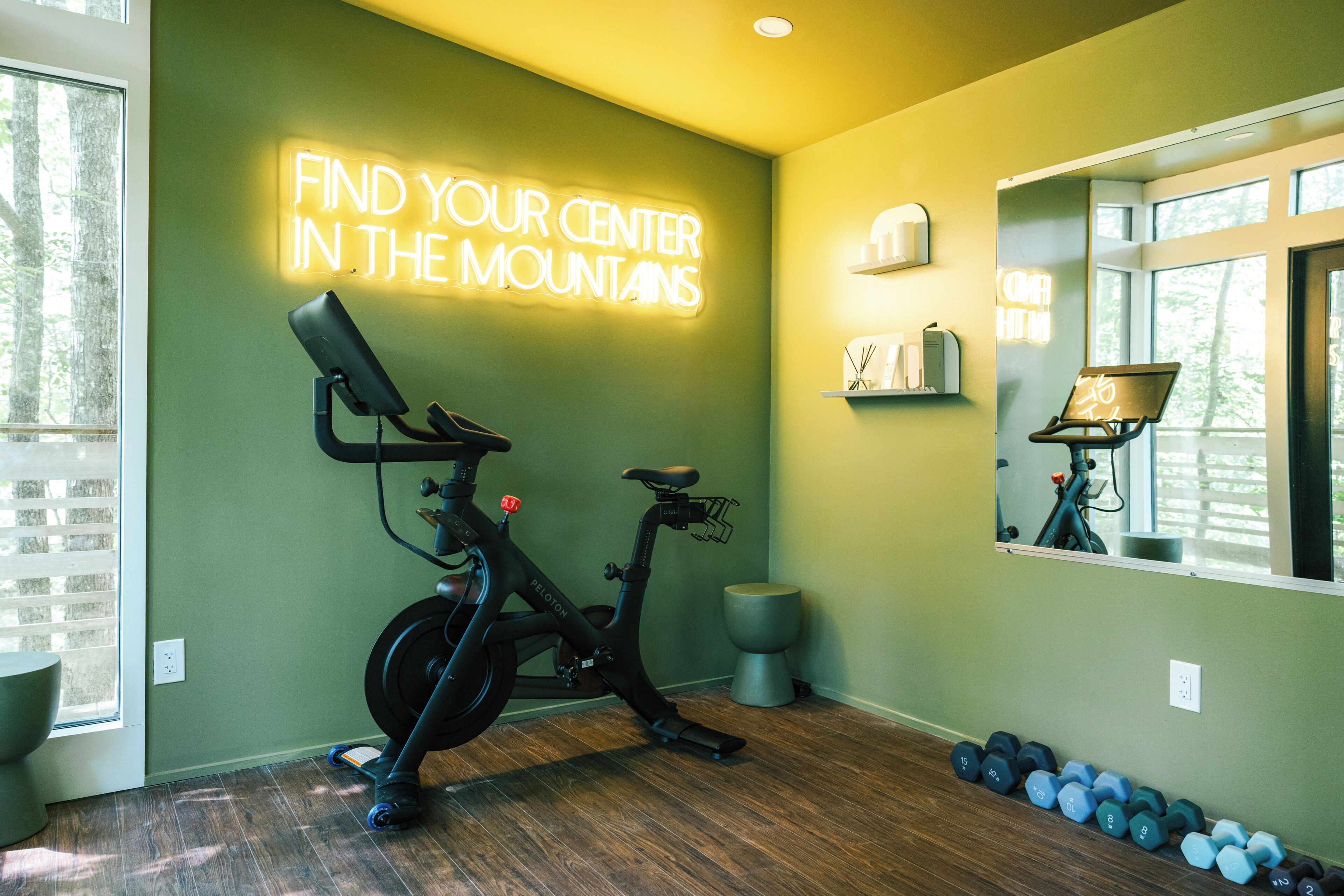 A gym with a stationary bike, dumbbells, and a neon sign.