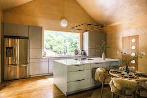 A modern kitchen with a large island, stainless steel appliances, and a view of greenery outside. - Havenridge Hideaway Retreat ~ Sauna ~ Cold Plunge ~ Gym ~ EV Charger ~ Pets (Cherry Log)