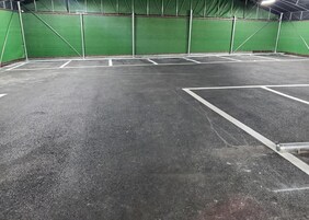 Una cancha deportiva interior con paredes verdes y piso oscuro, delimitada con líneas blancas.
