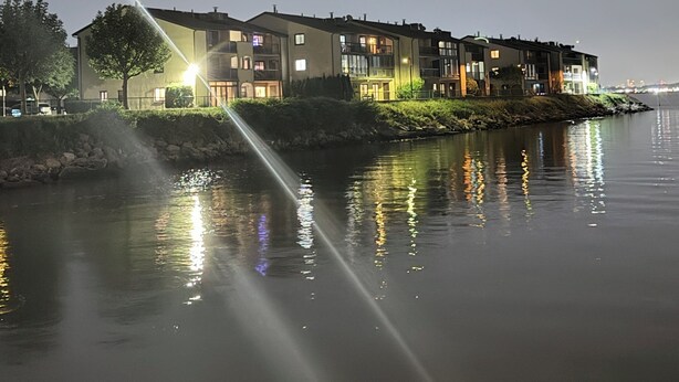 Un bâtiment situé au bord de l’eau, avec plusieurs étages, une étendue d’eau visible devant et une façade bien éclairée.